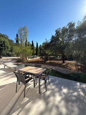 Eine Terrasse im Freien mit Tisch und Stühlen, umgeben von Bäumen und blauem Himmel.