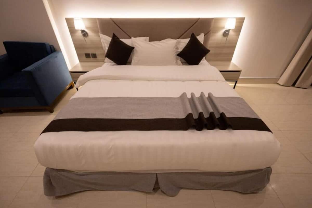 Una camera d'hotel moderna con un letto grande, comodini, un tavolino da notte e una poltrona blu.