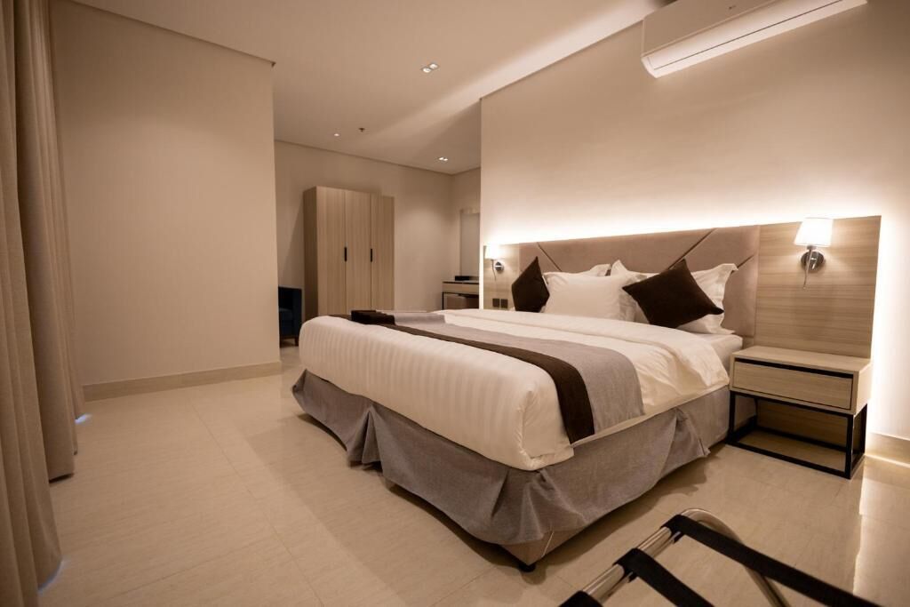 Una habitación de hotel moderna con una cama grande, mesitas de noche, un armario y un baño visible al fondo.