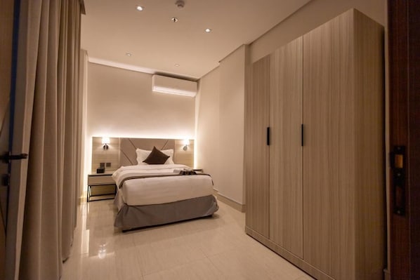 Una habitación de hotel moderna con cama, mesitas de noche, armario y aire acondicionado instalado en el techo.