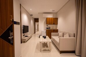 Un soggiorno moderno con divano, tavolino, televisione e angolo cottura con mobili in legno.