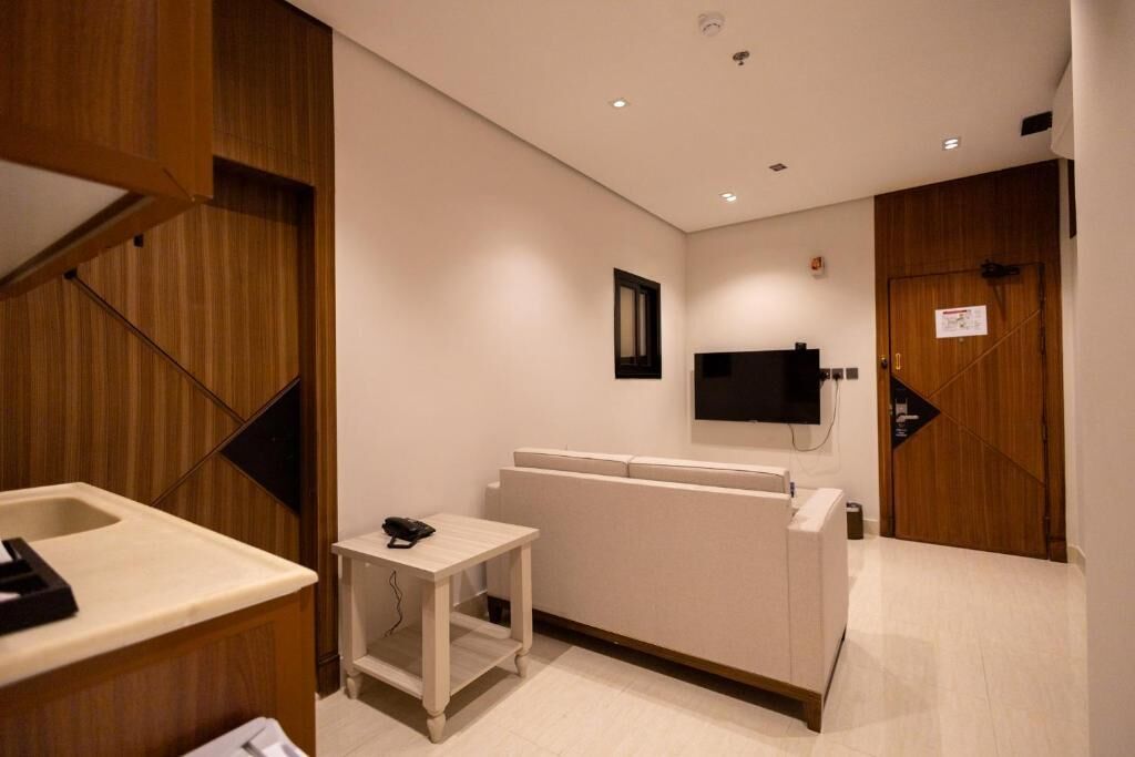 A hotel room with a wooden accent wall, a small bedside table with a phone, a flat-screen TV mounted on the wall, and a wooden door with a sign.