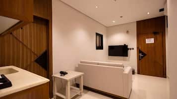 A hotel room with a wooden accent wall, a small bedside table with a phone, a flat-screen TV mounted on the wall, and a wooden door with a sign.