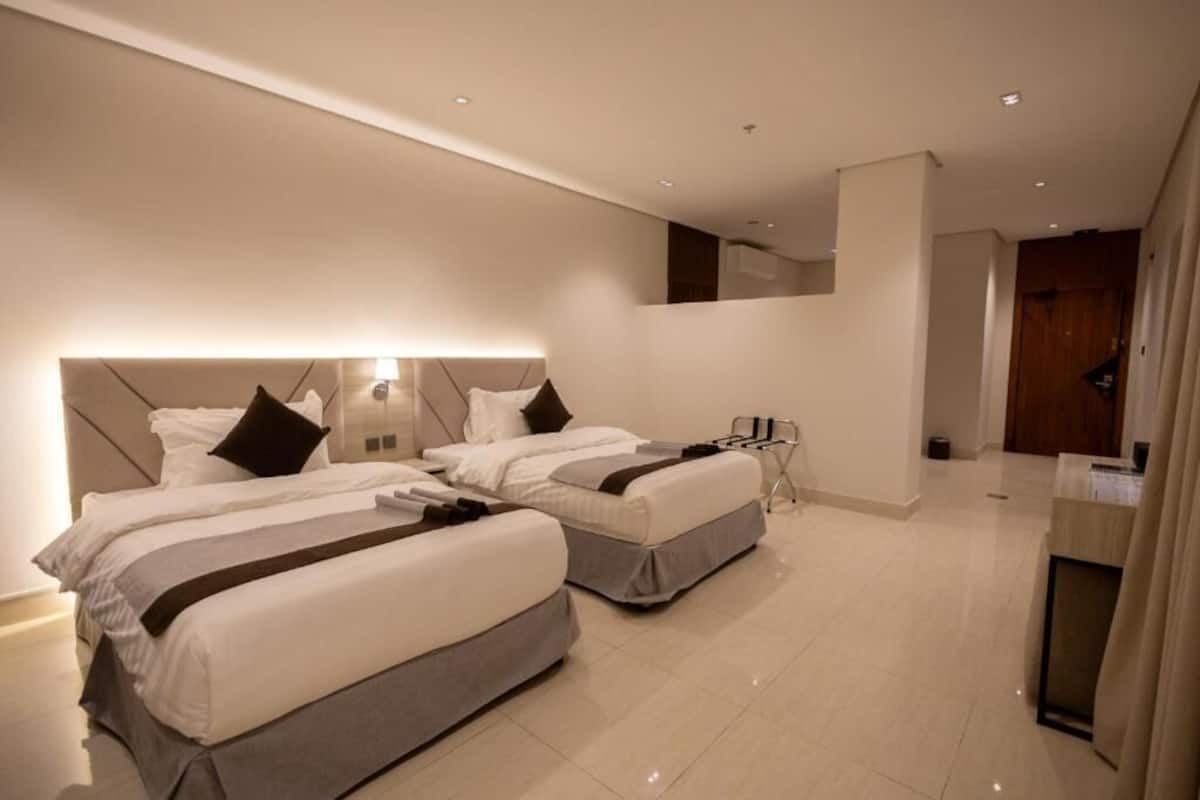 Una moderna camera d'albergo con due letti, un piccolo angolo salotto e uno specchio sopra i letti.