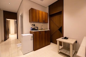 Cocina compacta con armarios de madera, un refrigerador pequeño y una mesa con un teléfono.