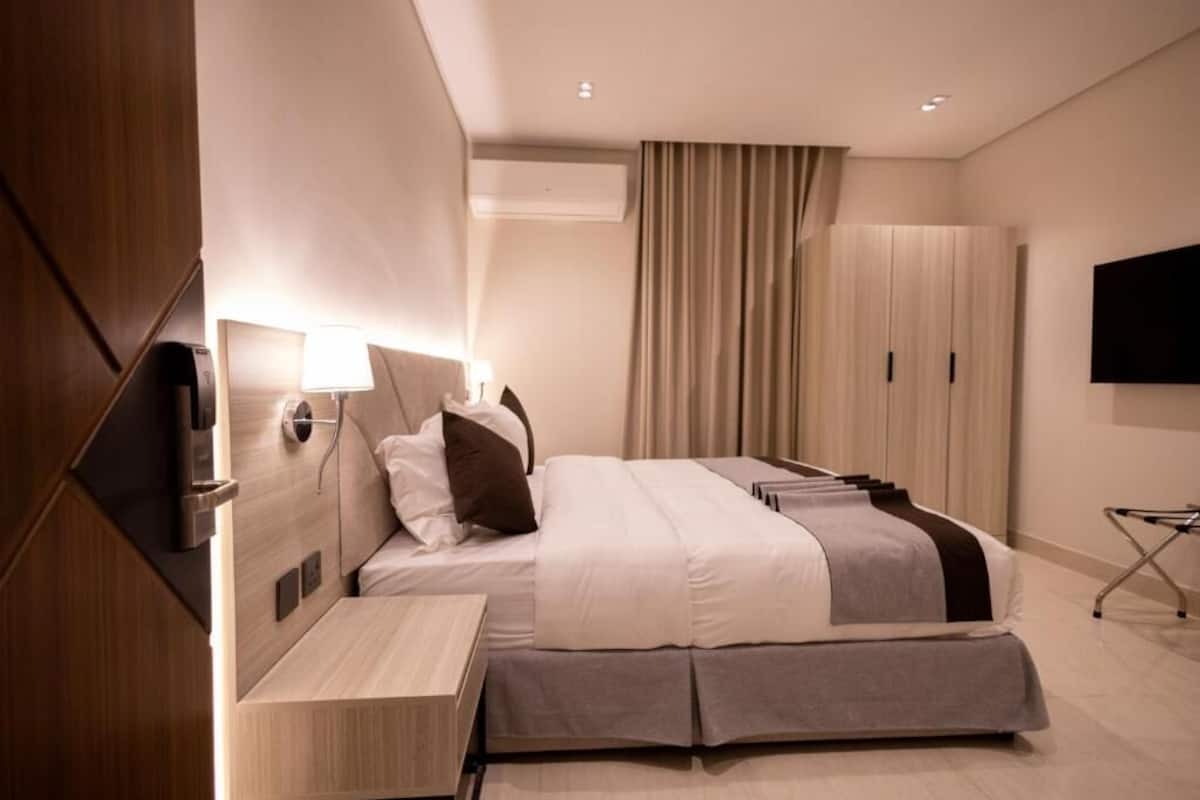Una camera d'albergo moderna con un letto, un comodino, una lampada, un condizionatore d'aria e una televisione.