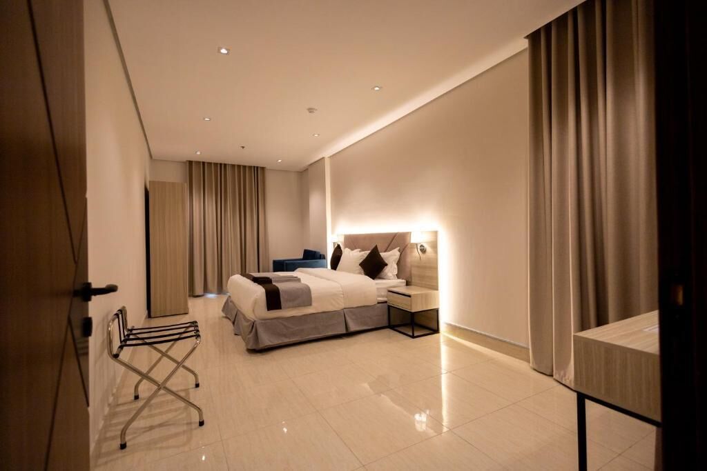 A modern hotel room with a bed, bedside table, lamp, and a small desk.
