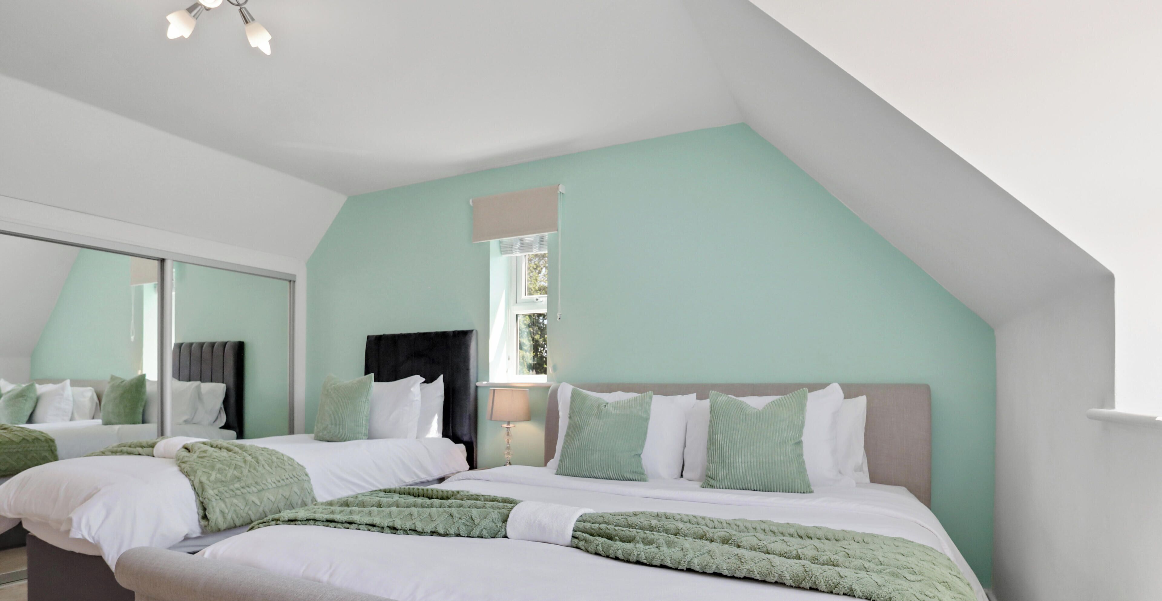 A bedroom with two beds, a window, and a mirror.
