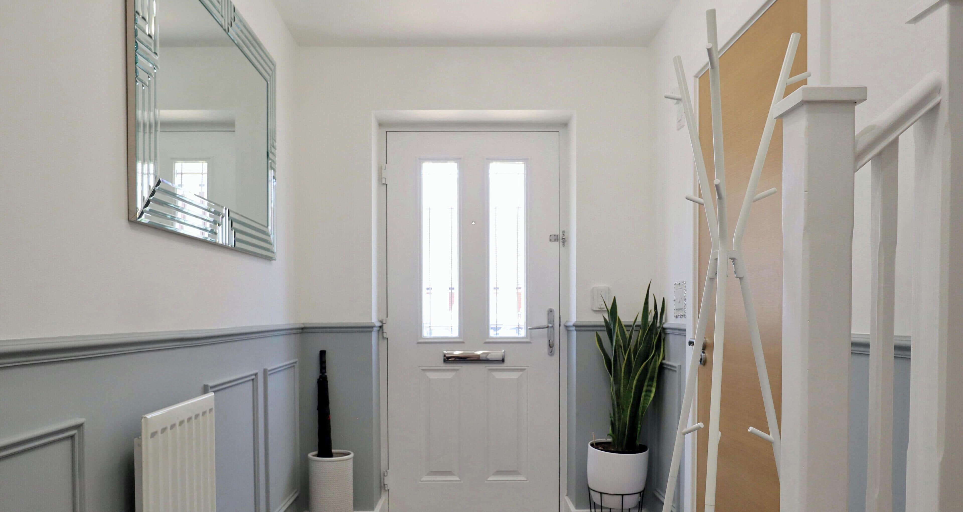 A hallway with a white door, a radiator, a potted plant, and a mirror on the wall.