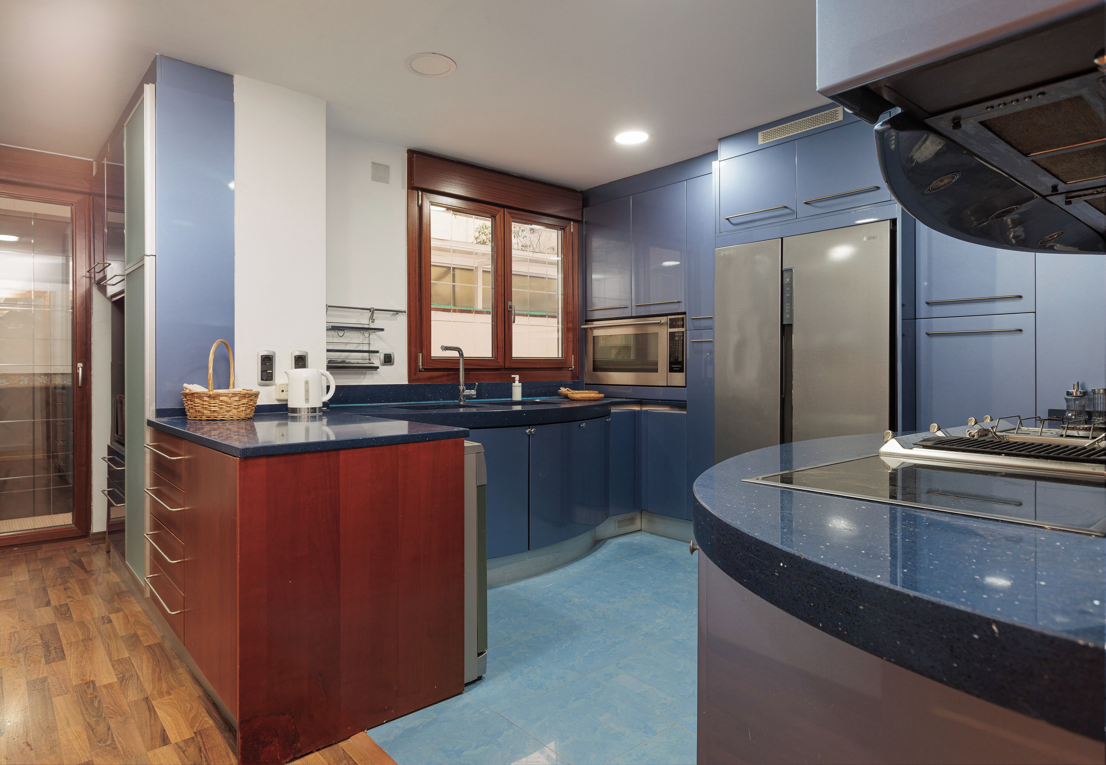 A modern kitchen with a built-in oven, a stainless steel refrigerator, and a blue countertop.