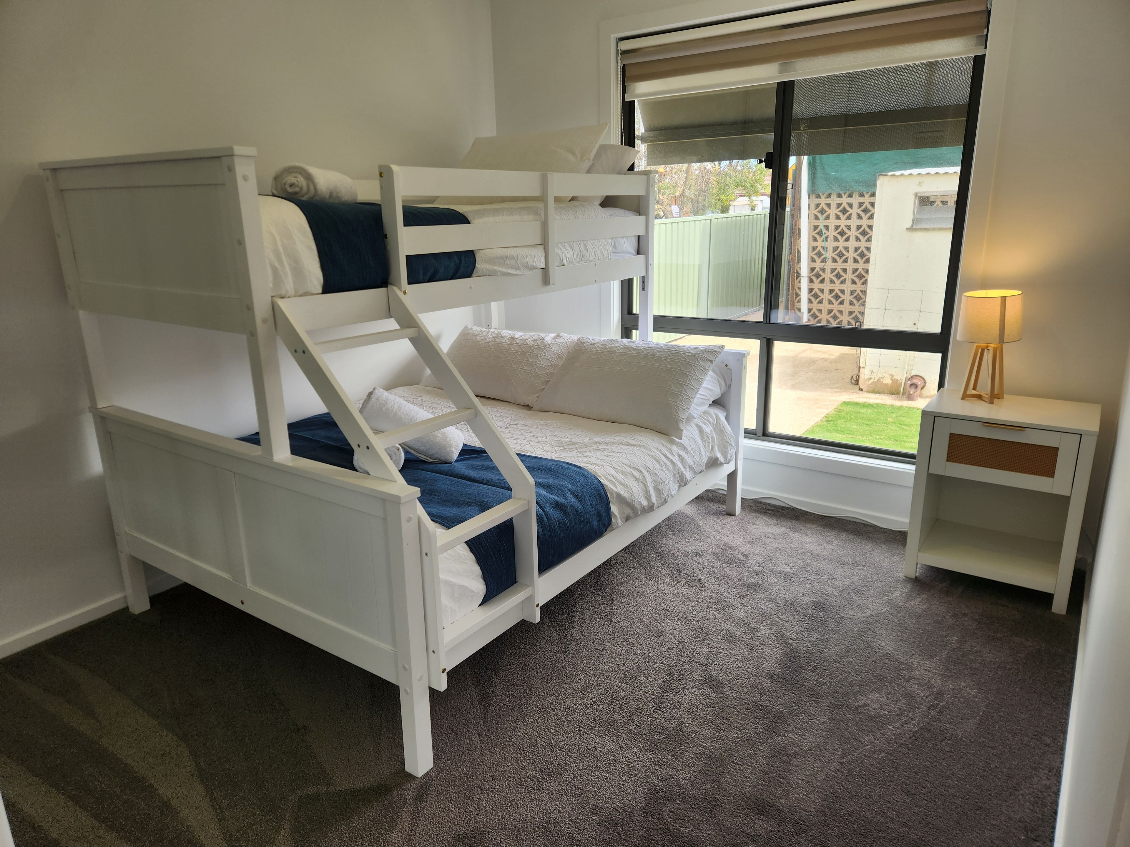 Ein Stockbett mit Schreibtisch und Lampe, ein Fenster mit Außenblick und ein Teppichboden.