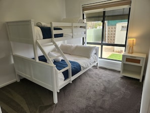 A bunk bed with a desk and a lamp, a window with a view of the outside, and a carpeted floor.