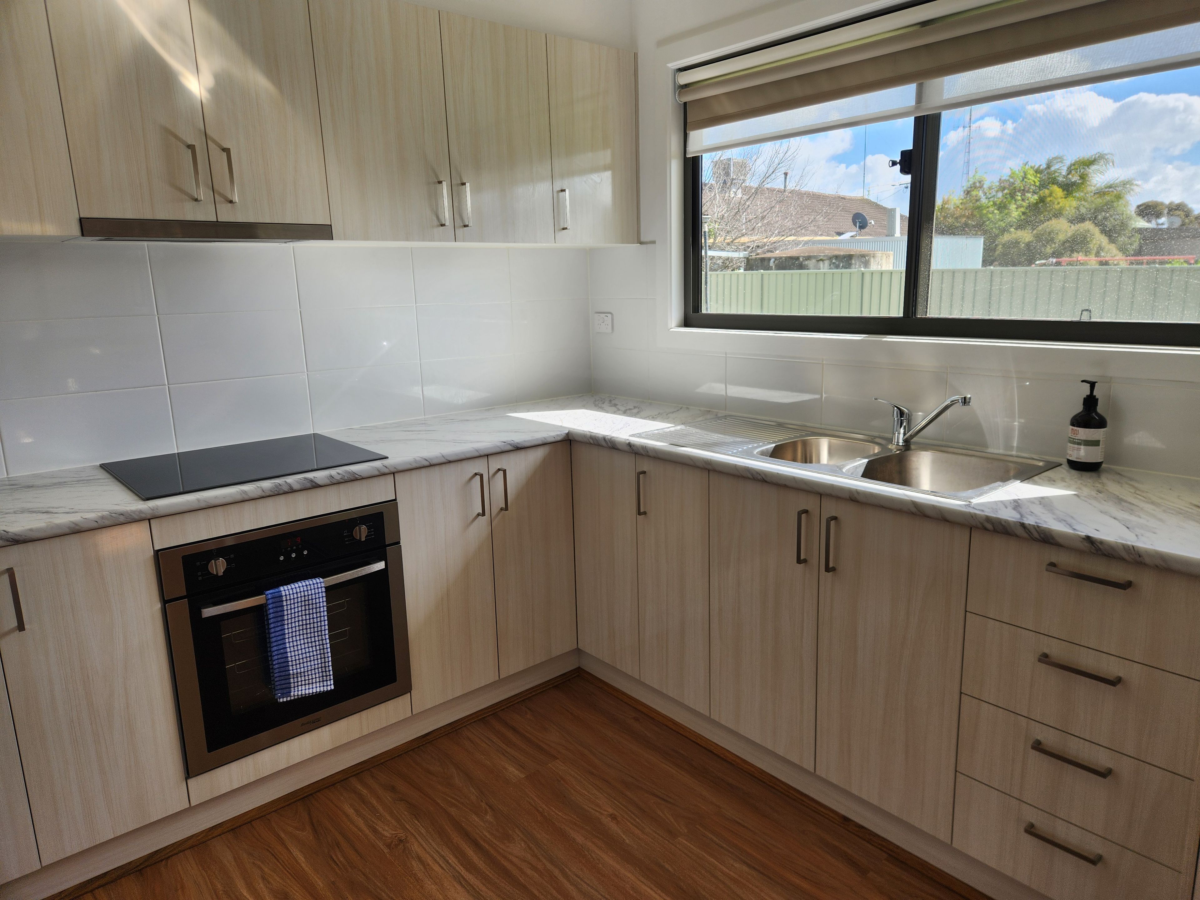 A modern kitchen with light wood cabinets, a stainless steel sink, and a built-in oven.