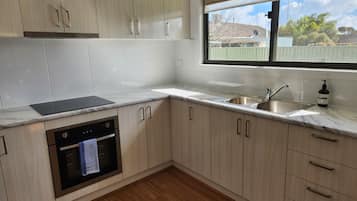 A modern kitchen with light wood cabinets, a stainless steel sink, and a built-in oven.
