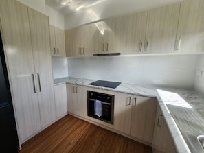 A modern kitchen with light wood cabinets, a built-in oven, and a marble countertop.