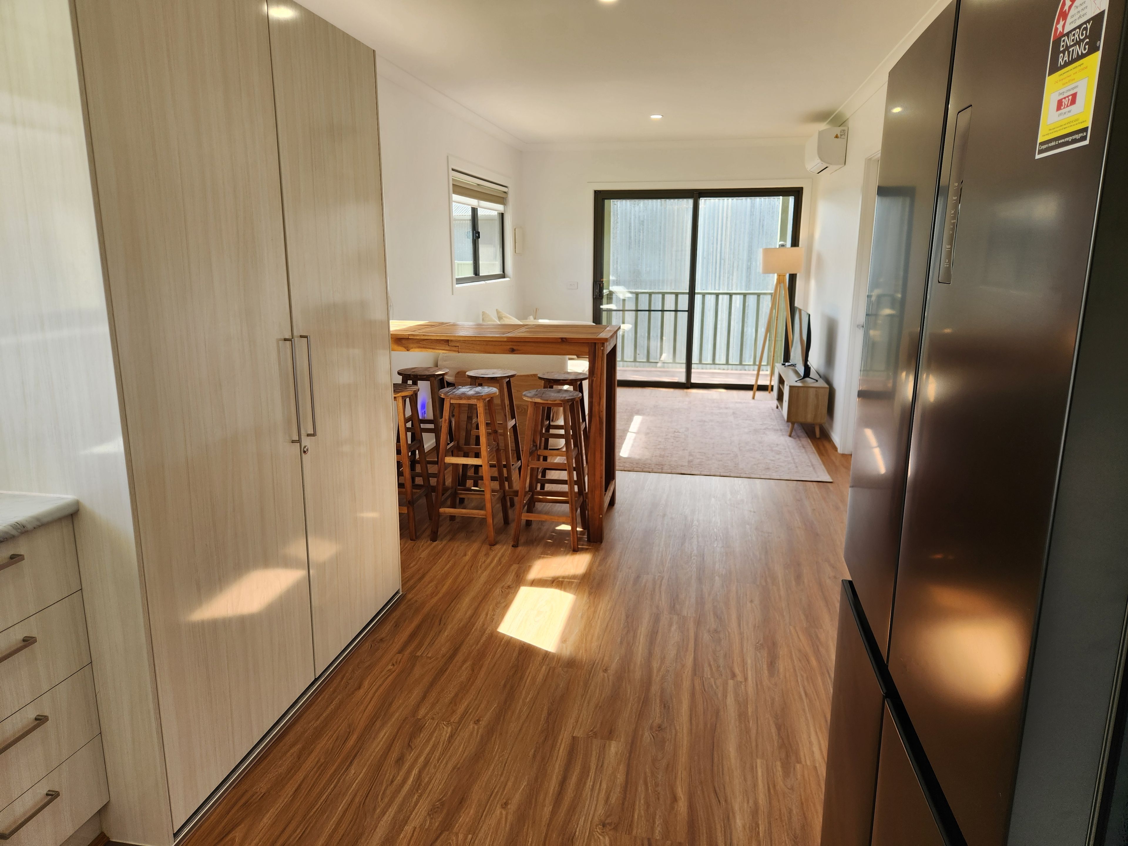 A modern kitchen with wooden flooring, a built-in refrigerator, and a dining area with stools.