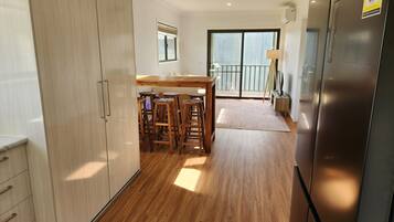 A modern kitchen with wooden flooring, a built-in refrigerator, and a dining area with stools.