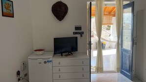 A room with a television on a white cabinet, a wall-mounted heater, and a door leading outside.