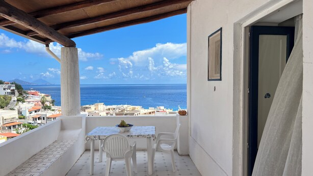 A balcony with a table and chairs, a view of the sea, and a cityscape in the background.