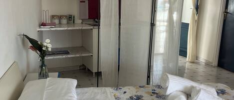 A hotel room with a bed, a bedside table, a vase with flowers, a wardrobe, a shelf with decorative plates, and a curtain.