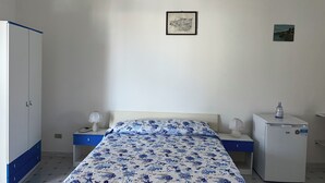 A bedroom with a bed, a wardrobe, a nightstand, a bedside table, a lamp, and a refrigerator.