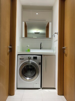 A compact laundry room with a washing machine, a sink, and a mirror above the sink.