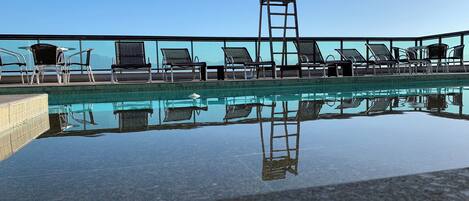 Una piscina con agua cristalina, rodeada de sillas de descanso y una escalera.