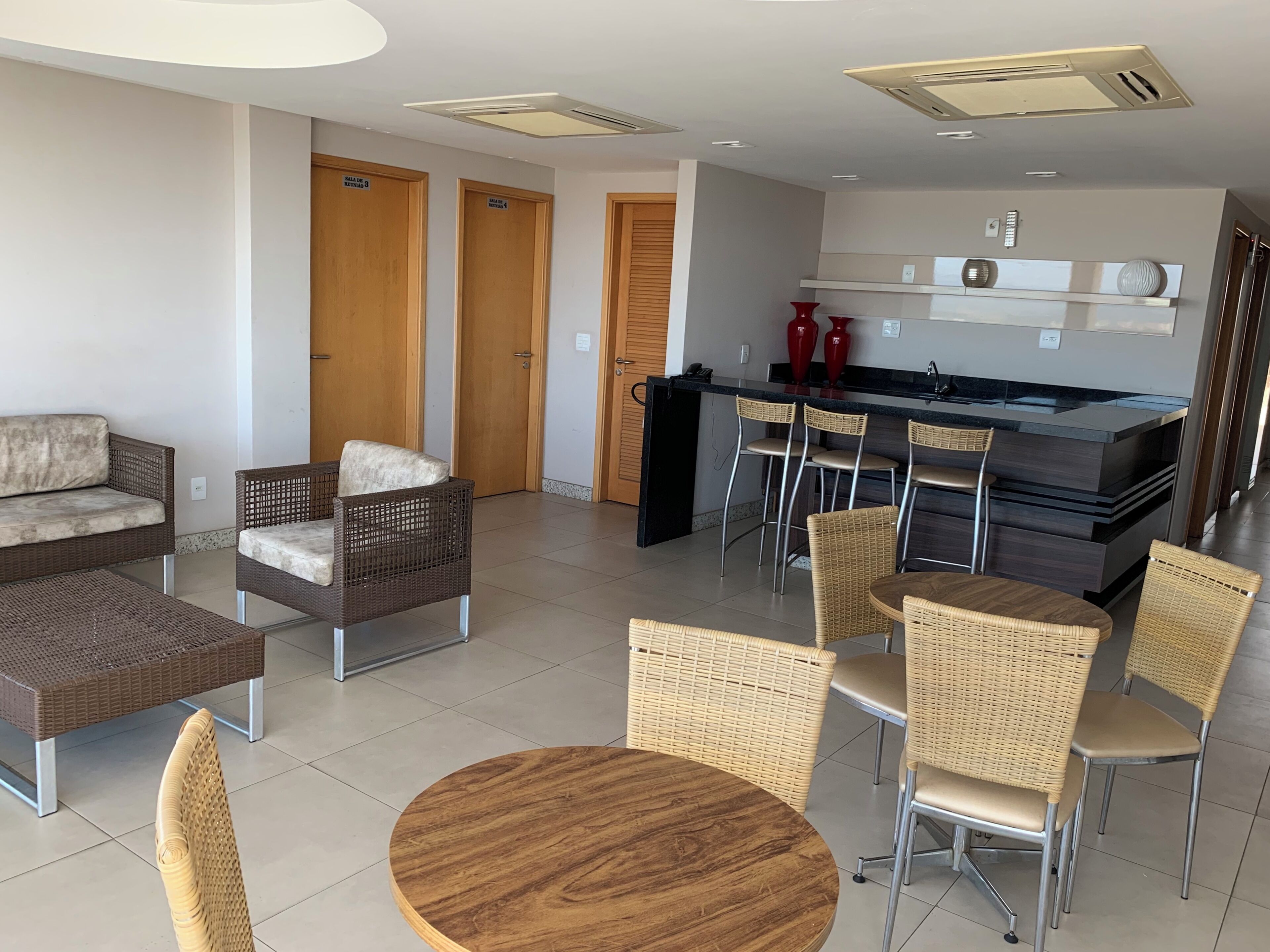A modern hotel room with a sofa, chairs, a dining table, a kitchen area, and a minibar.