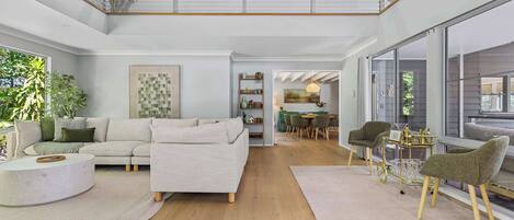 A spacious living area with a high ceiling, a dining area, and a view of the outdoors.