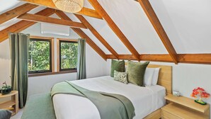 A bedroom with a sloped ceiling, a bed with pillows, a bedside table, and a window with curtains. - Private Kuranda Rainforest Villa with Pool (Kuranda)