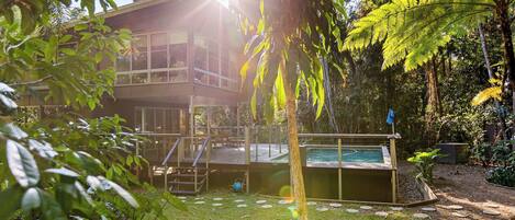 A two-story building with a pool, surrounded by lush greenery and a clear sky.