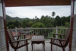 A balcony with two wooden chairs and a table, overlooking a lush green landscape with trees and hills.