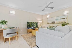 Ein modernes Wohnzimmer mit Flachbildfernseher, Deckenventilator und Essbereich mit Tisch und Stühlen.