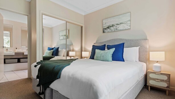 Quarto de hotel com uma cama grande, mesas de cabeceira, um espelho e um quadro na parede.