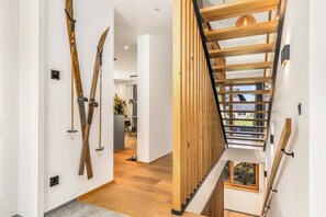 A modern interior with a wooden staircase, ski equipment on the wall, and a view of the outdoors. - Chalet with a terrace hot tub and sauna (Reit im Winkl)