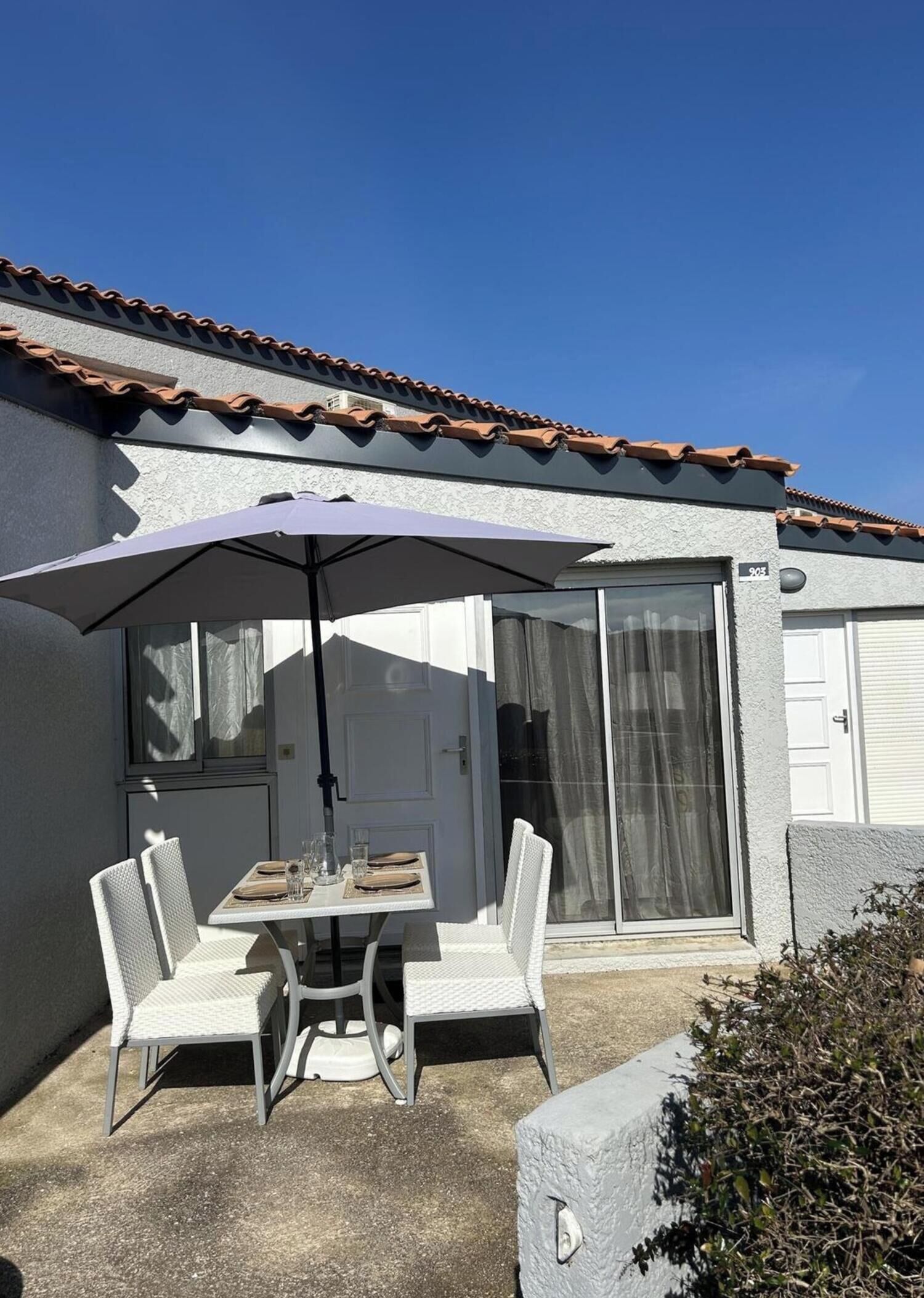A patio with a table and chairs, a covered umbrella, and a sliding glass door.