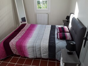 A bedroom with a bed, a nightstand, a lamp, a window, and a radiator. - FISHERMAN'S COTTAGE—Secluded on the SHORES OF LAKE St. Etienne, CANTAL, AUVERGNE—A UNIQUE EXPERIENCE (Lacapelle-Viescamp)