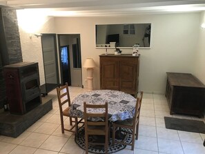 A dining area with a round table, chairs, a fireplace, a cabinet, and a mirror on the wall. - FISHERMAN'S COTTAGE—Secluded on the SHORES OF LAKE St. Etienne, CANTAL, AUVERGNE—A UNIQUE EXPERIENCE (Lacapelle-Viescamp)