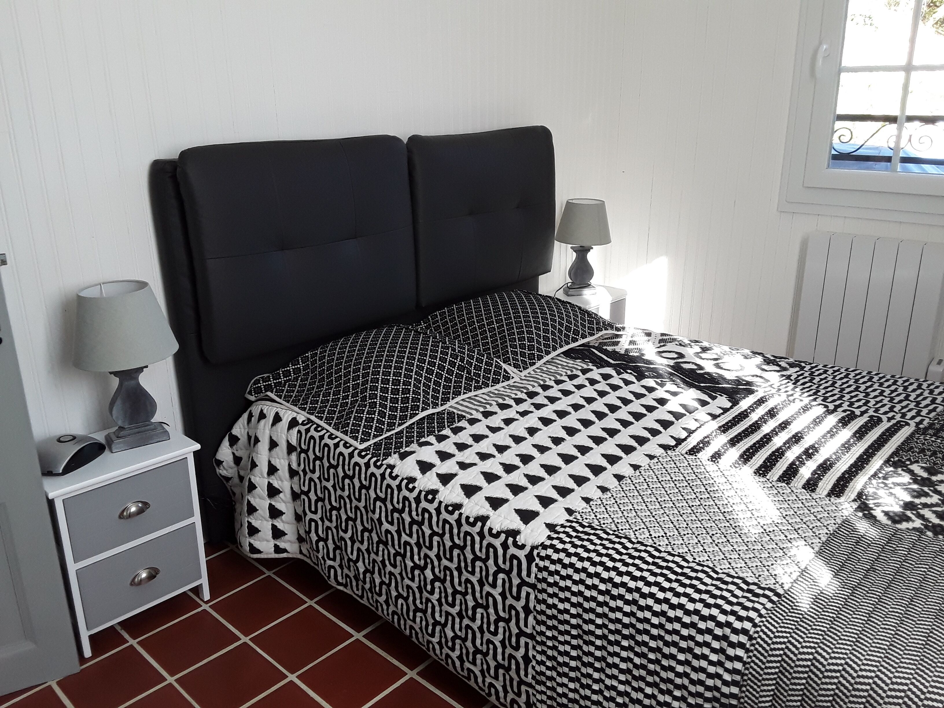 A bedroom with a bed, bedside lamps, a nightstand, and a window.