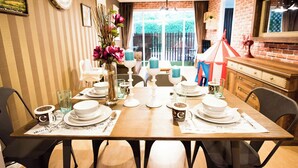 Un comedor con una mesa dispuesta para cuatro, sillas, un florero con flores y una pared de ladrillo.