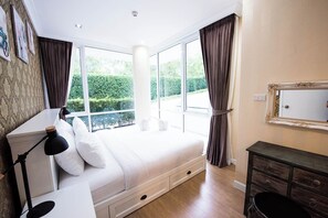 A bedroom with a large bed, a bedside table with a lamp, a dresser, and a window with curtains. - A107 Cozy 2-bedroom apartment with Playground near Beach (Nongkae)