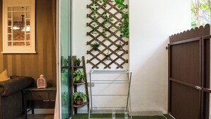 Una habitación con pared de celosía de madera, un tendedero metálico, un banco acolchado y una pequeña mesa con un farol.