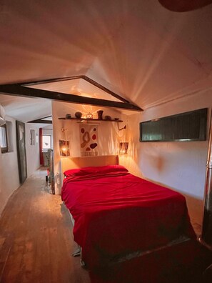Une chambre à coucher avec une couvre-lit rouge, une tête de lit ornée d’éléments décoratifs et un couloir menant à une autre pièce.