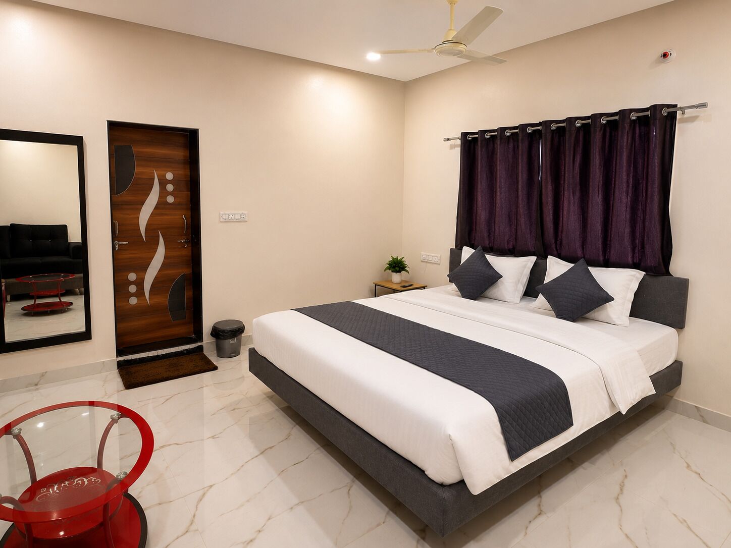 A modern bedroom with a bed, a ceiling fan, a nightstand, a potted plant, and a red chair.