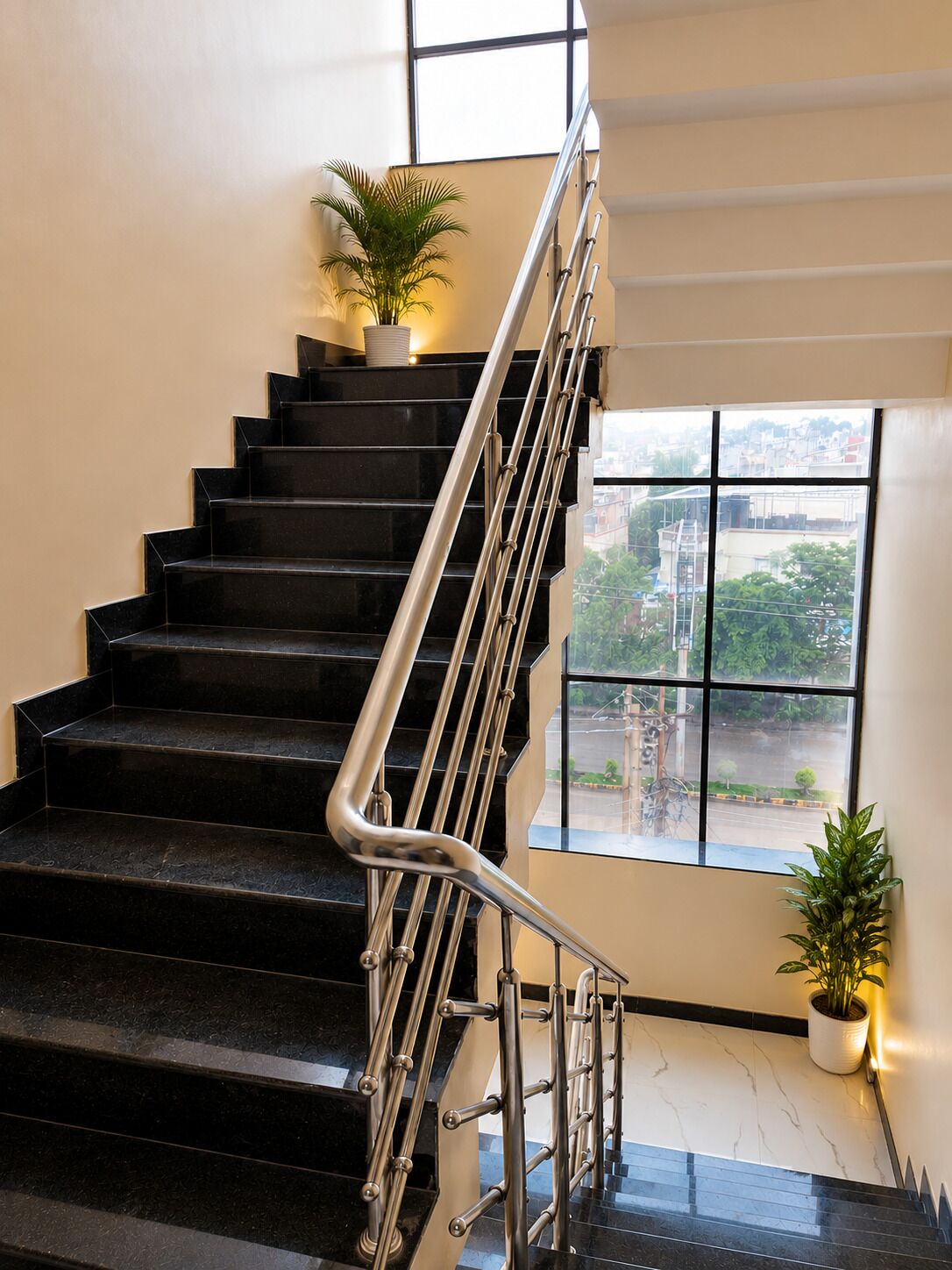 Una escalera con escalones negros y barandilla metálica, que lleva a un rellano con una planta en maceta.