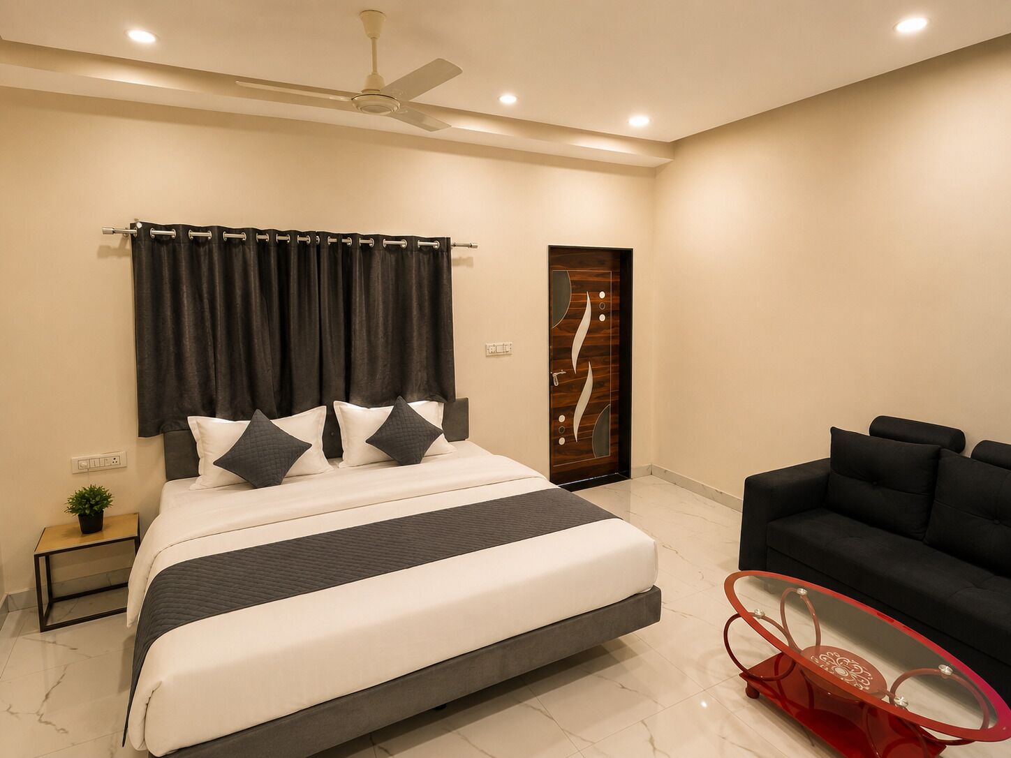 A modern bedroom with a large bed, a ceiling fan, a dark-colored door, and a black sofa.