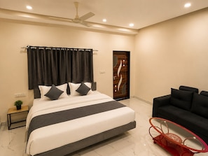 A modern bedroom with a large bed, a ceiling fan, a dark-colored door, and a black sofa.
