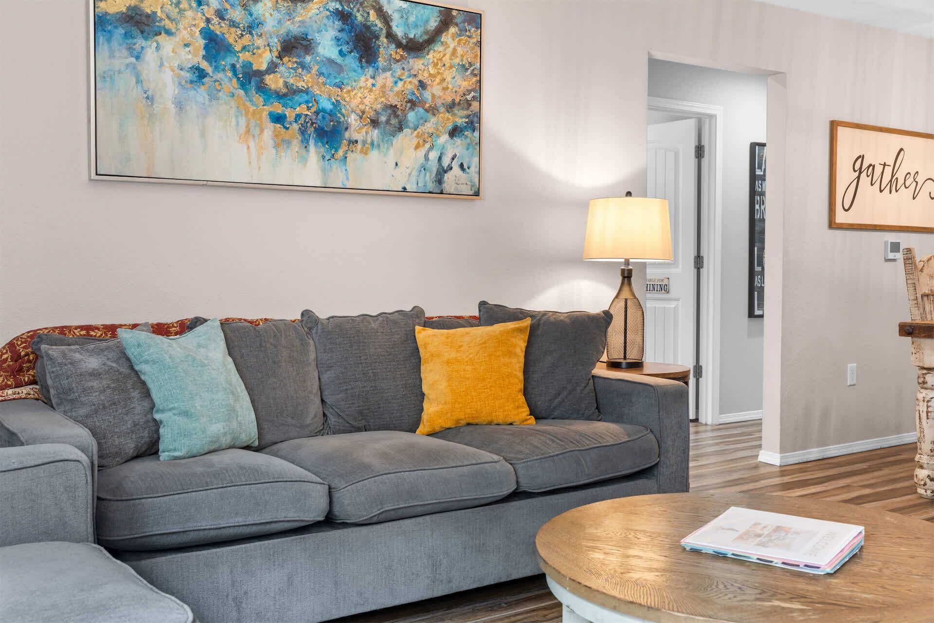 Ein Wohnzimmer mit grauem Sofa, einem Holztisch und einem Bild an der Wand.