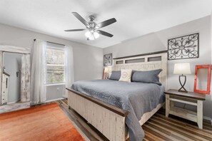 A bedroom with a bed, a ceiling fan, a window with blinds, a bedside table, and wall art. - SDC Escape Spacious Condo (Branson)