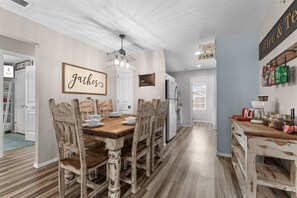 Ein Essbereich mit Holztisch und -stühlen, einer Chandelierleuchtre und einem Schild mit der Aufschrift 'gather'.